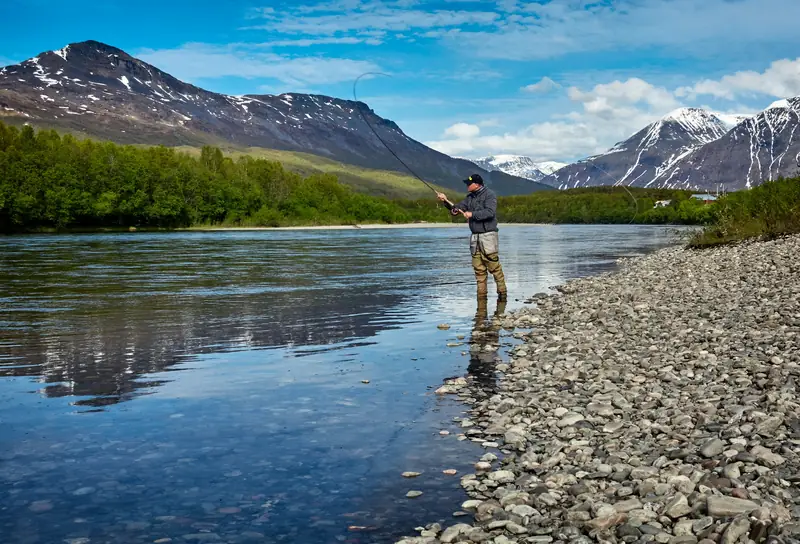 An angler wading a clear Montana river below snowy peaks